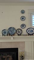 Seven blue and white collector plates displayed on a mantel with three on stands and others mounted above.