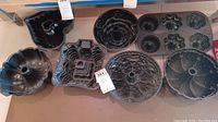Photo of eight black metal cake molds of various intricate shapes including heart, Bundt, tower, floral and scalloped patterns laid out on a surface