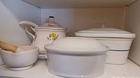 Photo showing the full set of ceramic ware including crocks, tureen, and mortar with pestle on a shelf.