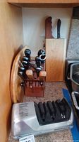 General view of two wooden knife blocks, a knife sharpener, and a wooden cutting board, all placed on a kitchen counter.
