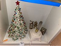 Ceramic Christmas tree and candle holders placed on a white shelf. Includes two metallic figurines of a reindeer and snowman nearby.