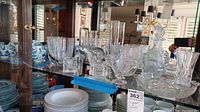 Multiple clear crystal items including a decanter, tall vases, bowls and serving pieces displayed on a glass shelf.