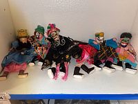 Six Asian finger puppets displayed on white shelf, showing varied traditional costumes and painted masks with detailed embroidery.