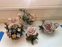 Grouped floral figurines including pink roses and a basket of flowers on a white surface.