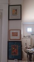 Three framed prints hanging on wall in a vertical display, showing variety of styles and frames.