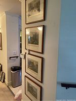 Four framed wall art prints hanging vertically on a light-colored wall, wood-tone frames, visible tags on two frames