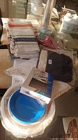 Overview photo showing folded kitchen towels, disposable plates, plastic cups, pot holders and box of forks on table.