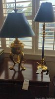 Photo showing a brass base lamp with a tripod claw foot design and a black lampshade.