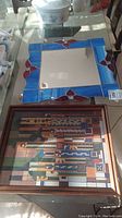 Photo showing a stained glass framed mirror with blue border and red floral motifs alongside a framed stained glass graphic artwork with geometric lines and shapes.