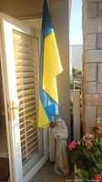Ukrainian flag hanging next to a door and garden statue at the base