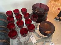 Photo showing multiple cranberry colored stemmed wine glasses and water goblets grouped on a glass table with cranberry colored plates and bowls behind them.