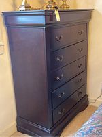 View of tall boy dresser showing full height and side profile; dark finish with a wide top and base molding.
