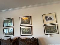 Photo showing six matted and framed wall art prints hung in two rows above a dark cushion, with some reflections on glass.