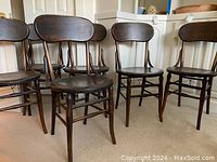 Front view of six dark-stained wooden bentwood dining chairs arranged in a row.