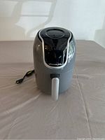Front view of PowerXL air fryer showing gray body with black top, cord on table, and front handle.