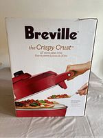Front of the box showing the brand Breville, model The Crispy Crust, 12-inch stone pizza oven with a picture of the oven and pizza.