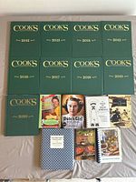 Group photo of 15 cookbooks including Cook's Illustrated annual editions from 2012 to 2020 and assorted other cookbooks with various covers and moderate wear.
