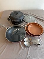 Overview of group cookware items including Gotham Red frying pan, Simply Ming frying pan, Miracle Maid pot, lids, and scoops.