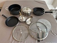 Full set overview on table showing pots, pans, lids, splatter guards, and utensil holder