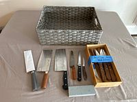 Gray woven basket, set of knives with wood handles, knife sharpener, and wooden box of Brazilian steak knives on table