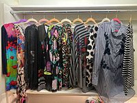 Multiple ladies tops on hangers showing various patterns and colors including bright multicolored floral, black faded floral, polka dot, and stripe patterns