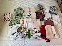 Photo showing a collection of worn dish towels and oven mitts with various colorful patterns laid out on a bed.