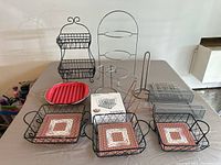 Full view of several kitchen racks and baskets arranged on a table including multi-tier racks, ceramic tile-insert baskets, and wire baskets.