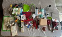 Photo showing a large variety of kitchen gadgets including peelers, slicers, cutters, measuring spoons, and ice cream scoop all laid out on a table.