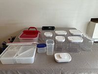 Wide view of miscellaneous plastic food storage containers with lids in various shapes and sizes arranged on a table.