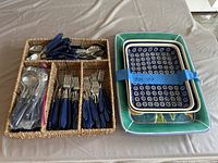 Blue-handled flatware and three ceramic trays on table; flatware organized in wicker tray with compartments