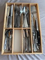 Set of Oneida flatware in wooden organizer tray showing knives, forks, spoons, and serving utensils.
