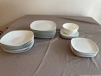 Photo displaying the full set of plain white dinnerware including multiple sizes of plates and bowls arranged on a table.