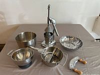 Photo showing the full set of kitchen items on table, including the juice squeezer, food mill, mixing bowls, steamer basket, and chopper with wooden handles.