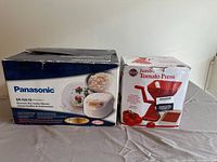 Original boxes for Panasonic rice cooker warmer and jumbo tomato press displayed side by side.