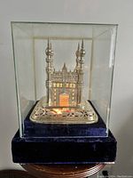 Front view of the silver plated mosque lamp in glass case, showing illumination and detailed architecture.