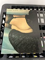 Cover of the Helmut Newton White Women book showing a rear view of a woman in black lingerie against a muted blue background.