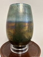 Full view of the vase-shaped art glass lamp with its colour gradient and Lucite base visible on a round wooden surface.