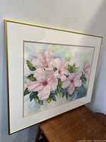 Image showing framed watercolor artwork of pink hibiscus flowers on a table against a wall.
