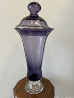 Full view of purple lidded mantle vase on wooden pedestal.