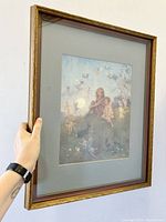 Framed art print held upright showing the print and shadow box frame with a gold carved border and gray mat.