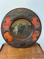 Front view of circular wooden plaque with painted pyrography scene of three Cossacks on horseback, showing silvered metal accents around the frame with missing decorative jewels.