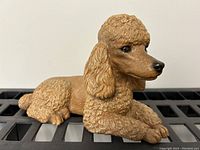 Front side view of the tan poodle figurine, showing detailed curly fur texture, facial features, and front paws