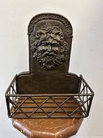 Front view of the heavy metal wine bottle holder rack showing a detailed Bacchus Satyr face relief and lattice basket.
