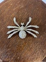Close-up photo of the vintage rhinestone spider brooch on a wooden surface showing detailed rhinestone decoration.