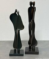Front view of two Boris Kramer hand-forged steel sculptures on a flat surface against white wall showing abstract human figures, one 10-inch and one 12-inch tall.
