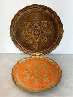 Photo of two vintage Italian Florentine round trays, one larger and one smaller, both with scalloped edges and gold leaf designs.