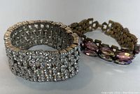 Photo showing two vintage rhinestone bracelets side by side. One wide clear rhinestone bracelet and one with pink and iridescent oval stones.