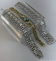 Three vintage rhinestone bracelets displayed on a clear acrylic stand showing the different styles.