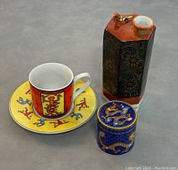 Top and angled views of lot including Keith Haring espresso cup with saucer, Asian porcelain sake bottle, and Chinese cloisonne trinket box