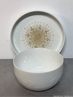 White porcelain serving bowl with raised wave pattern in front of decorative tray with gold mandala pattern.